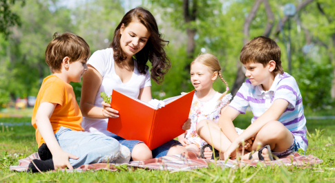 Kozzi-teacher-reads-a-book-to-children-in-a-summer-park-487-X-266.jpg